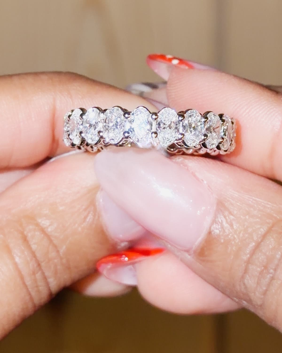 A white gold eternity band of oval lab grown diamonds set north south, held between fingertips