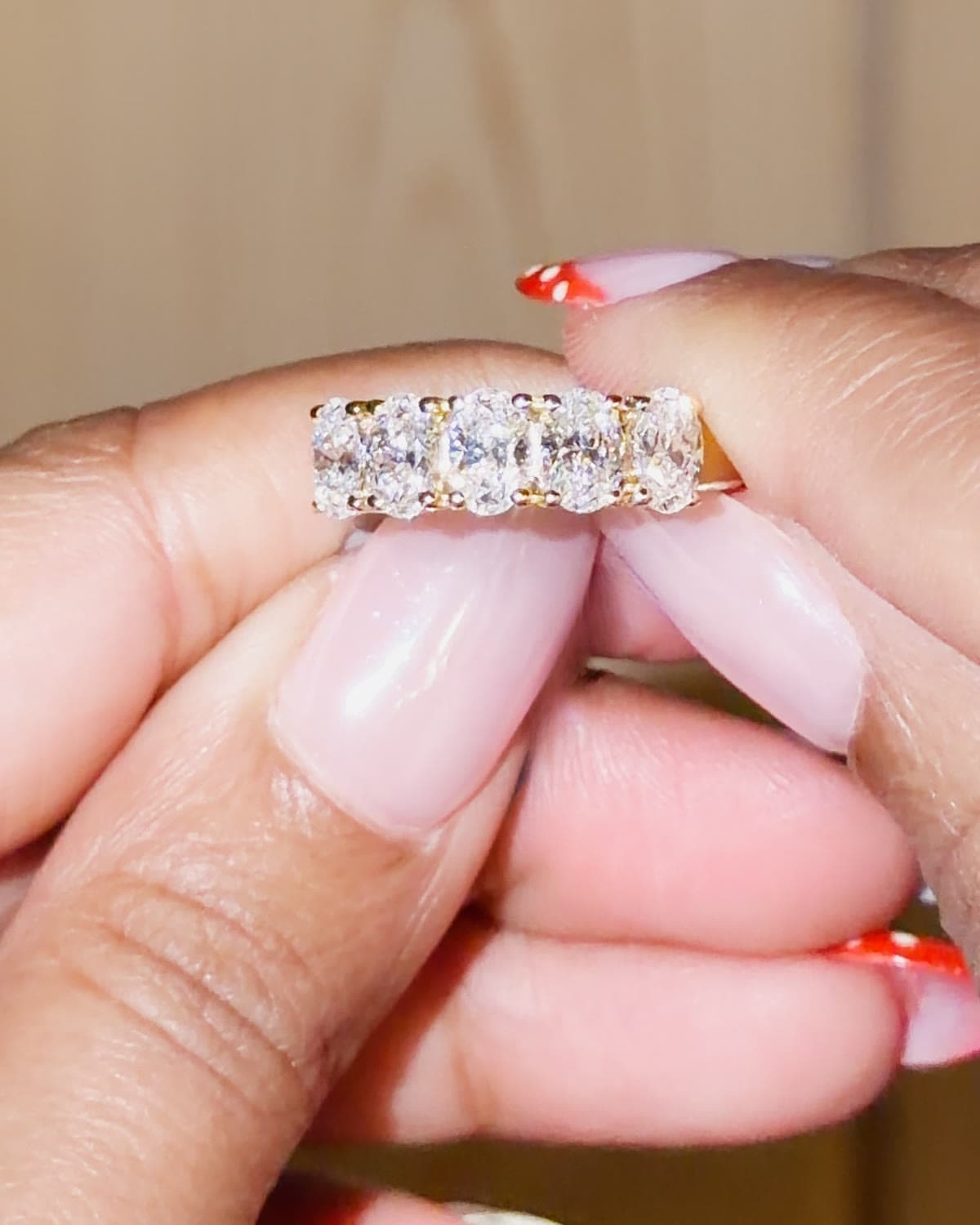 A yellow gold band with a row of oval lab grown diamonds set across the top, held between fingertips