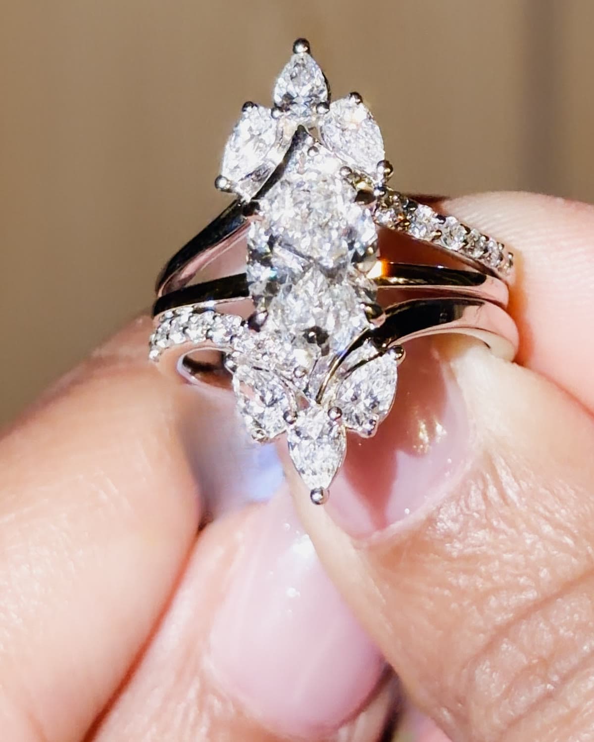 A 2.3 carat oval lab grown diamond engagement ring inside a white gold jacket of marquise and pear diamonds, held between fingertips