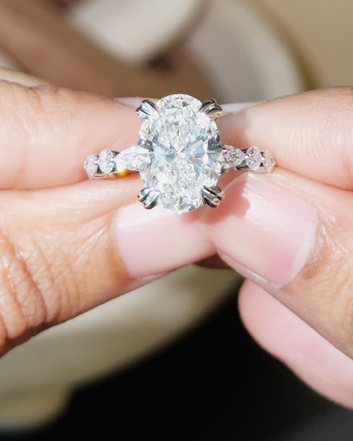 A 4 carat oval lab grown diamond engagement ring on a bubble band of round diamonds, held between fingertips