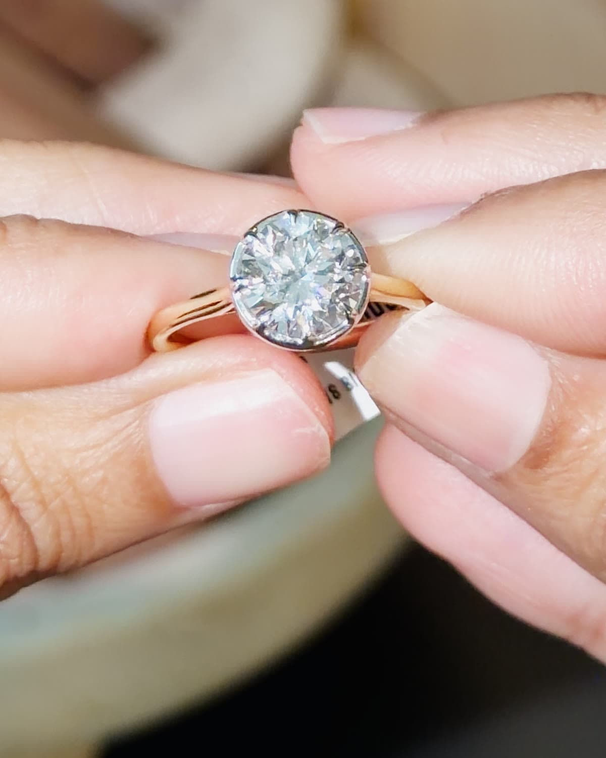 A 2 carat GIA certified natural round diamond engagement ring in yellow gold, held between fingertips
