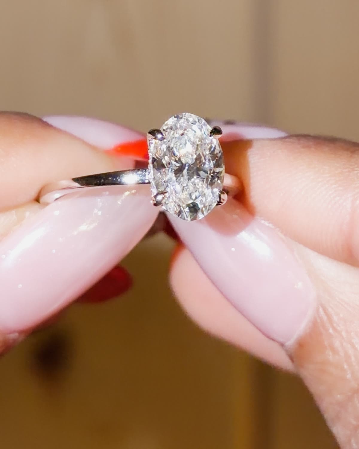 A 2.3 carat oval lab grown diamond solitaire engagement ring with double prongs in white gold, held between fingertips