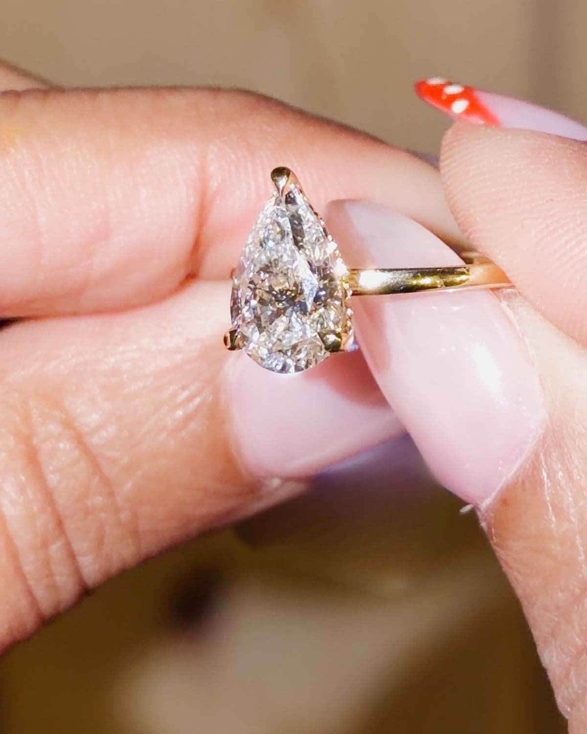 A 2.4 carat pear shaped lab grown diamond solitaire engagement ring in yellow gold, held between fingertips
