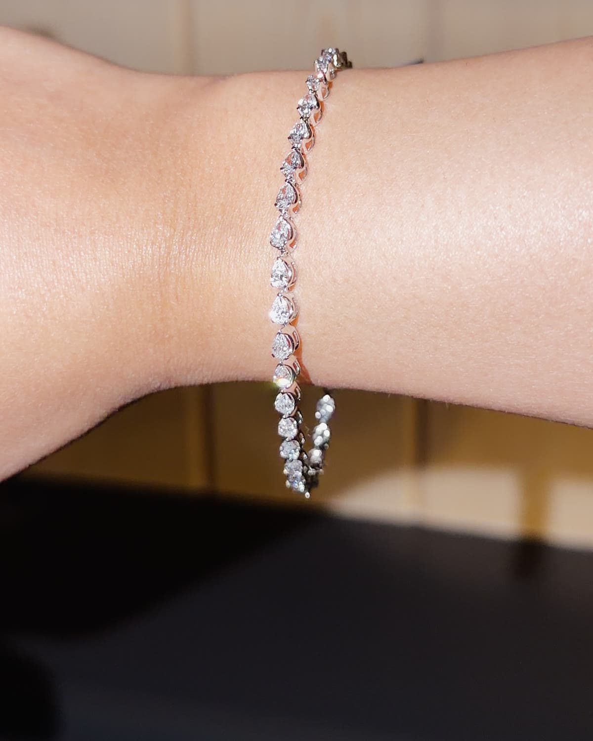 A white gold tennis bracelet of pear shaped lab grown diamonds set east west, worn on the wrist