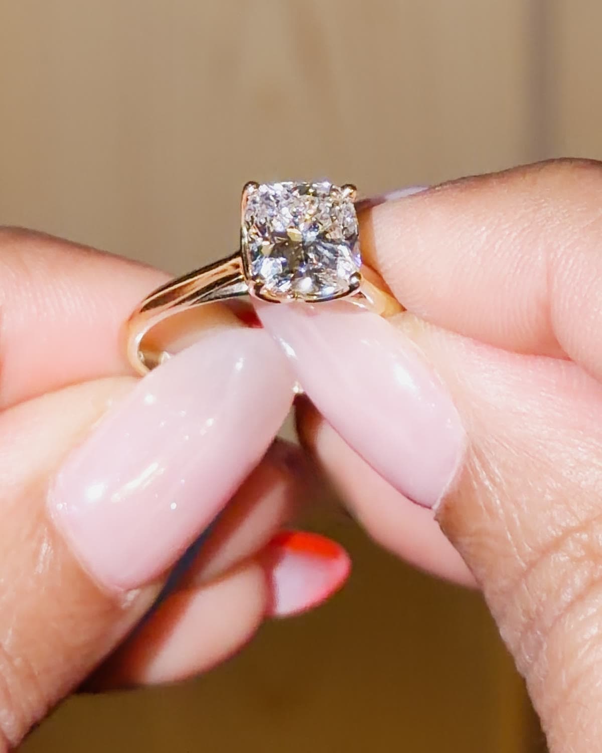 A 3 carat cushion cut lab grown diamond solitaire engagement ring in yellow gold, held between fingertips