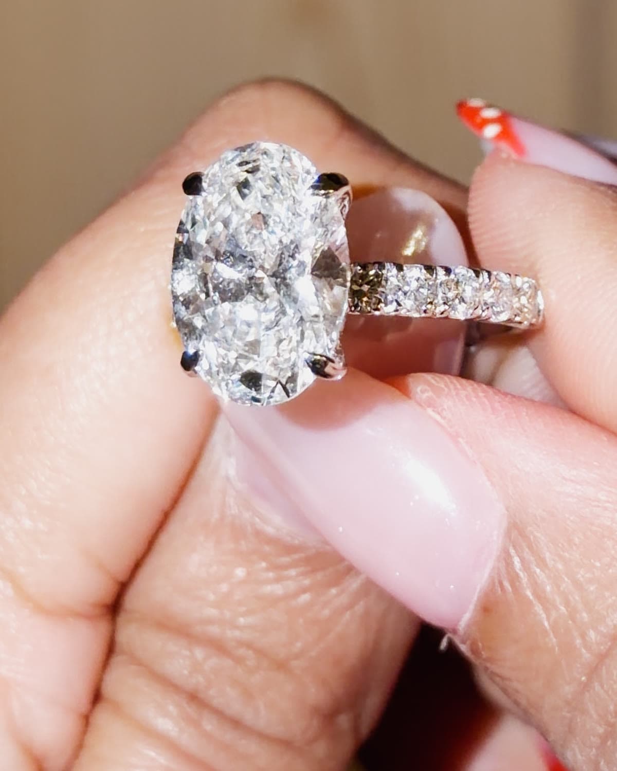 A 3.5 carat oval lab grown diamond engagement ring with a pavé band in white gold, held between fingertips