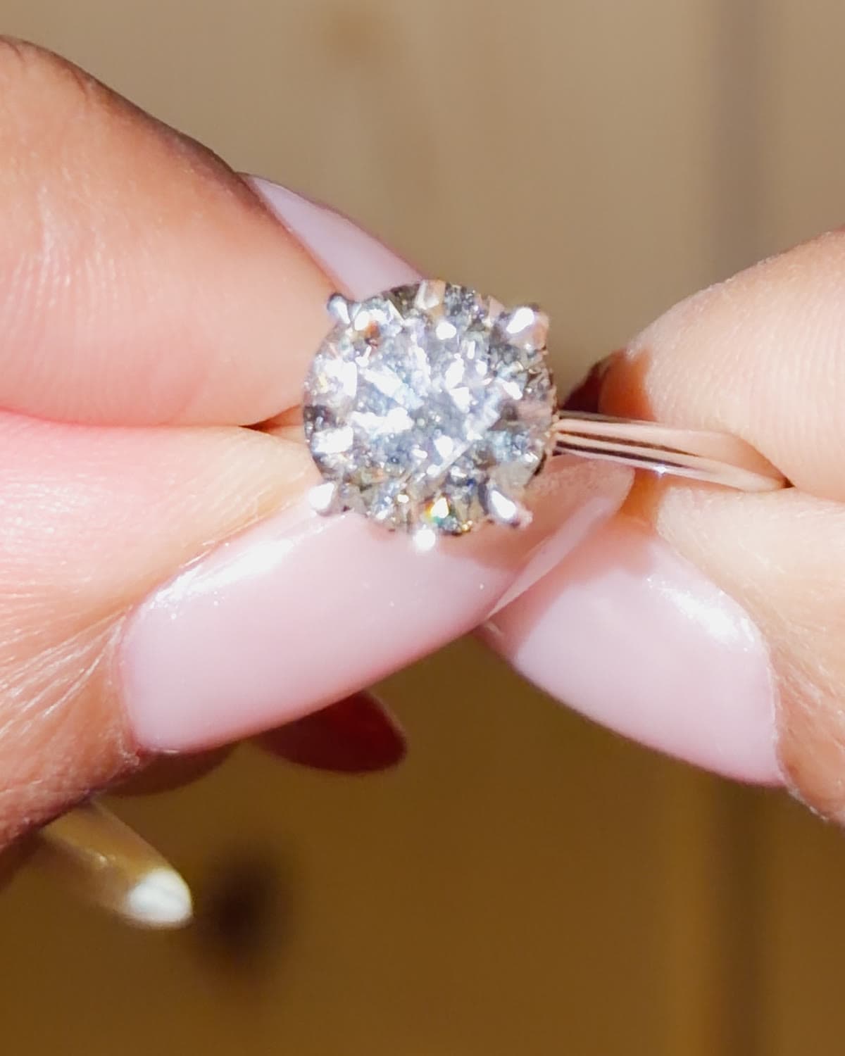 A 2.2 carat round brilliant lab grown diamond solitaire engagement ring on a plain white gold band, held between fingertips